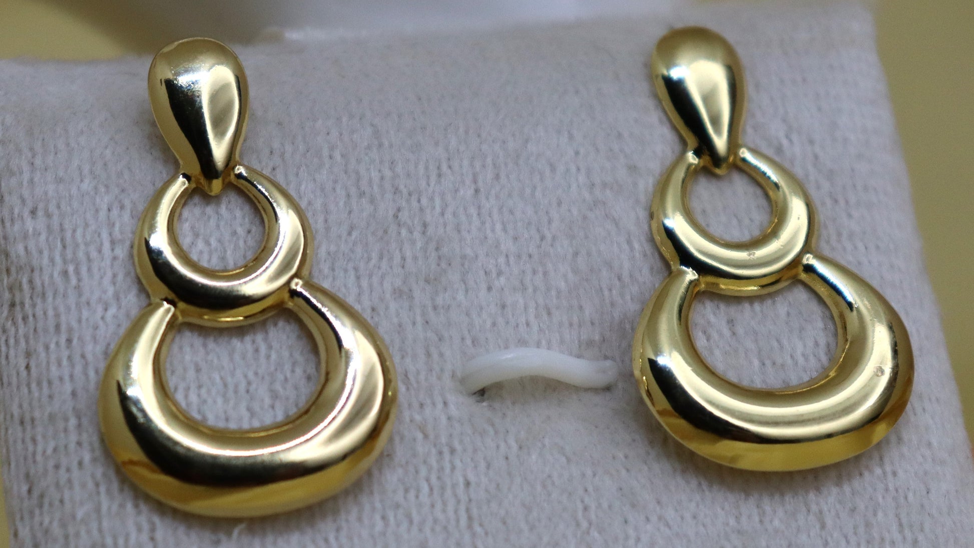 Pair of gold earrings on a white card with a blurred background