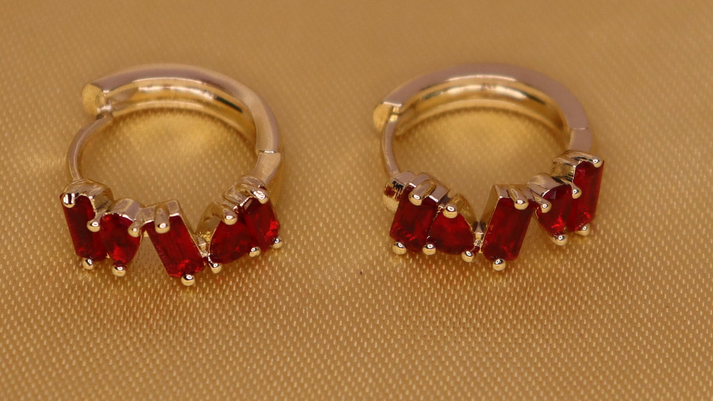 Gold hoop earrings with red gemstones on a beige fabric background