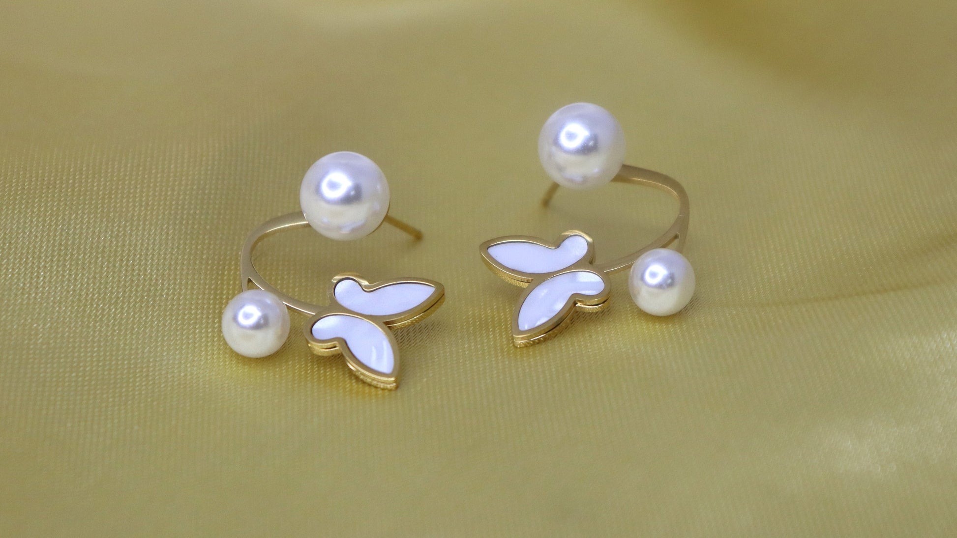 Pair of pearl earrings on a light yellow fabric background