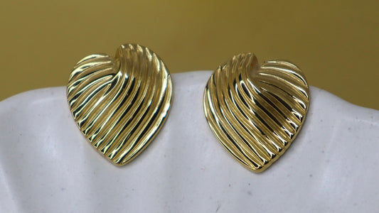 Gold heart-shaped earrings on a white shell with a beige background