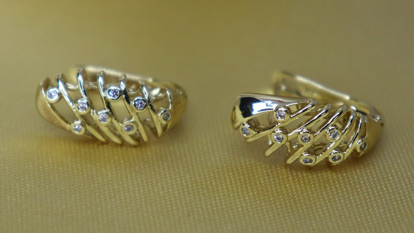 Pair of gold hoop earrings on a beige surface with a white object in the background.