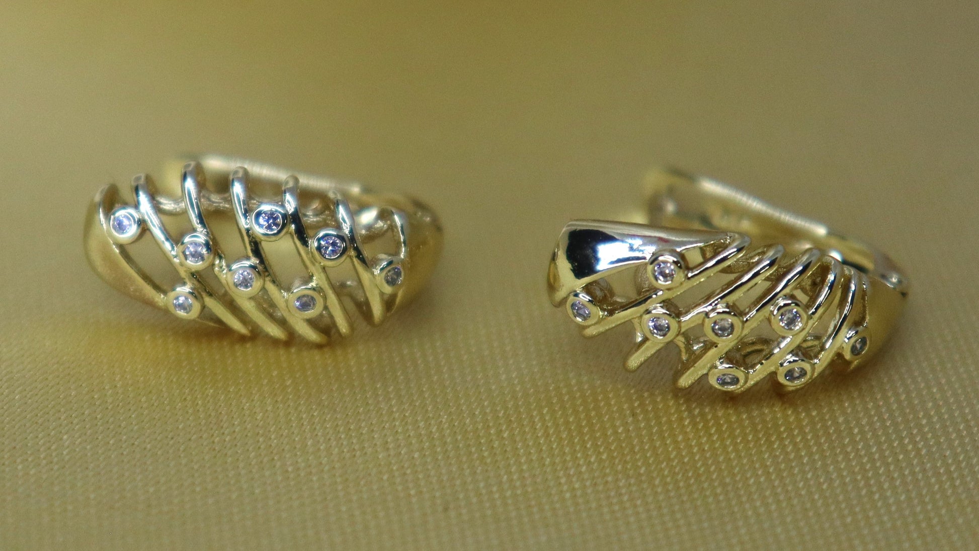 Pair of gold hoop earrings on a beige surface with a white object in the background.