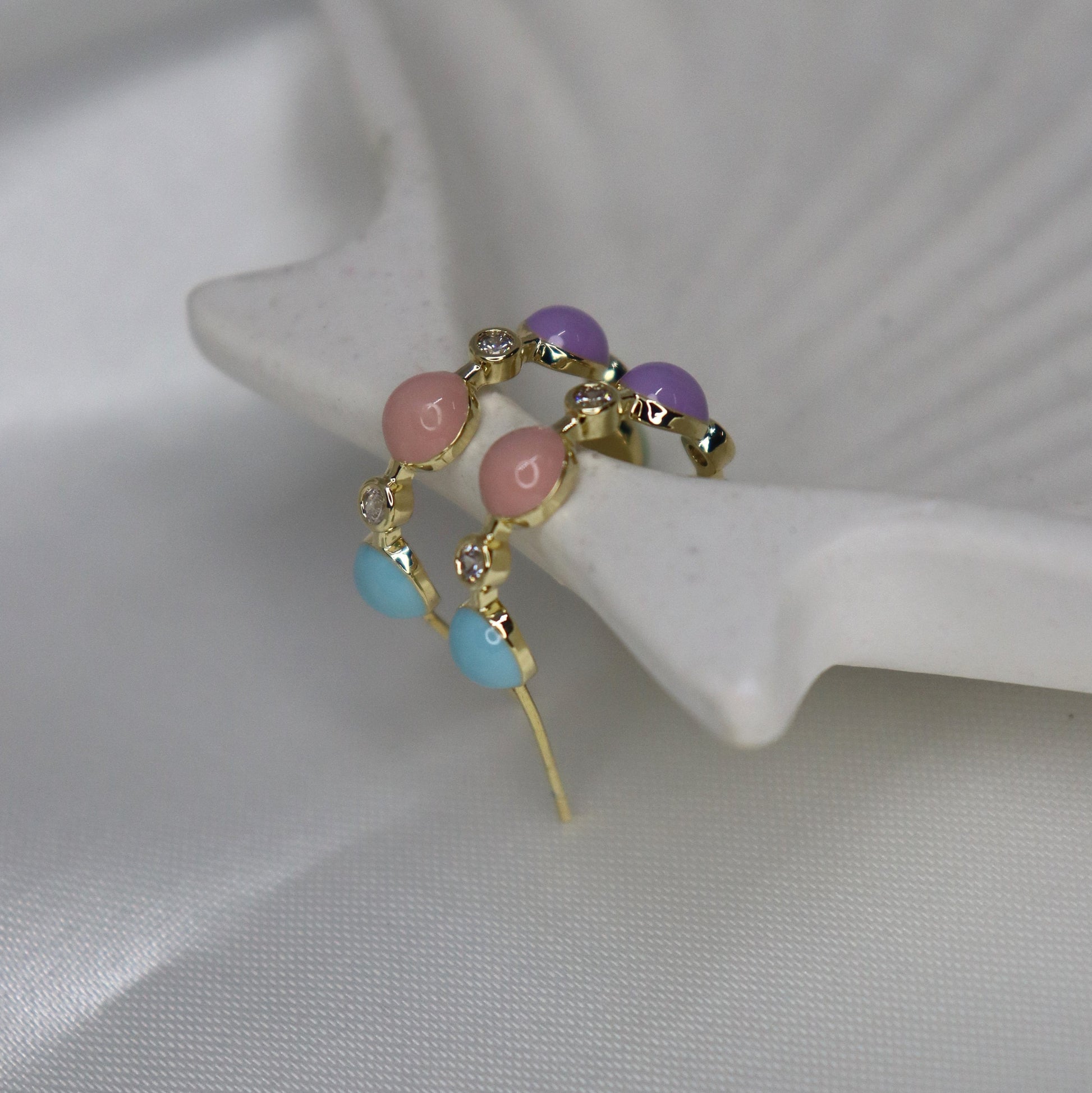 Gold earring with colorful beads on a white shell background