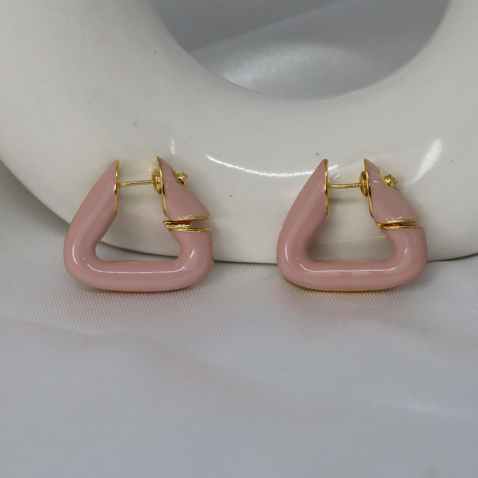 Pink hoop earrings with gold accents on a white surface.